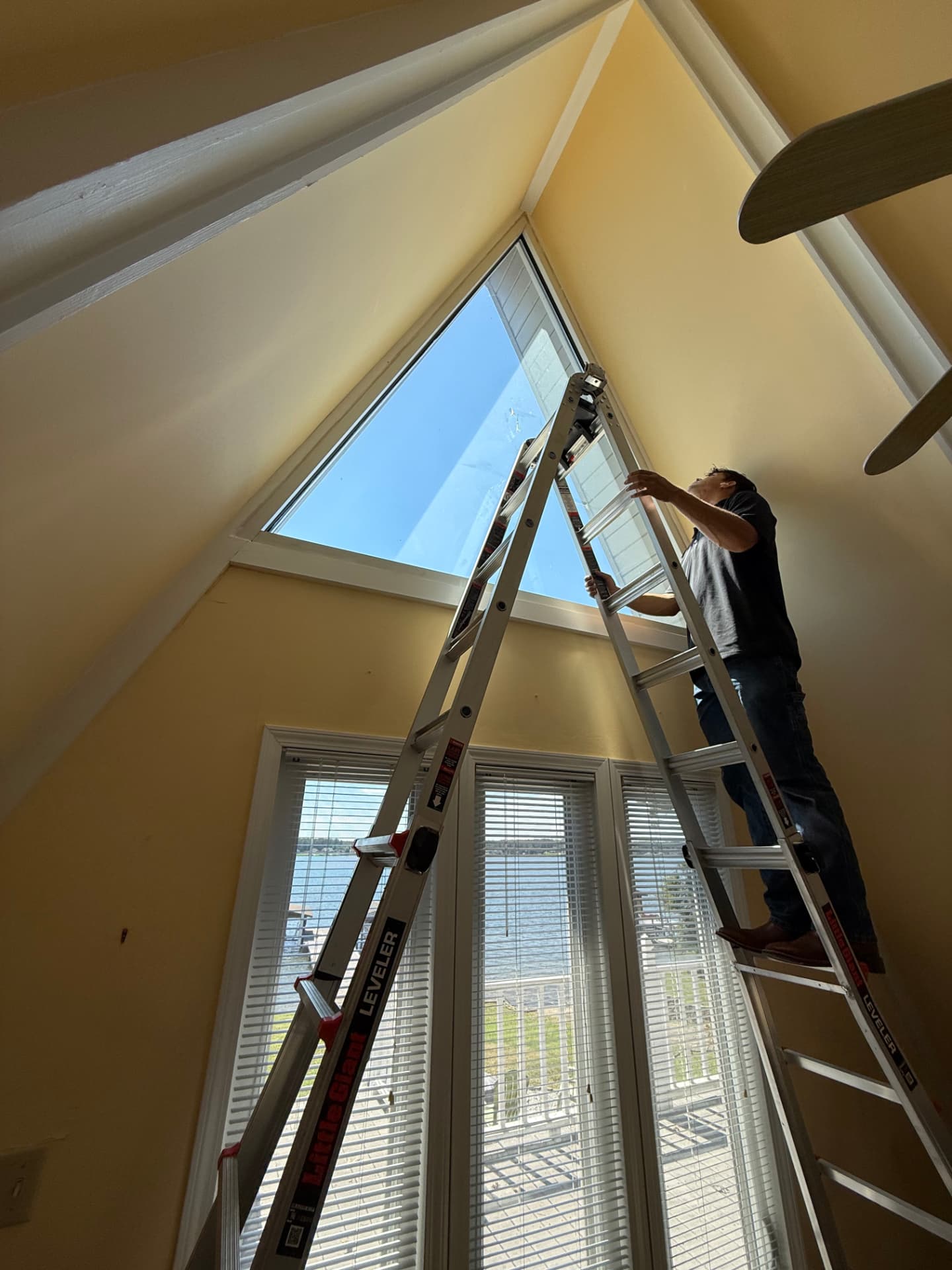 Installer on a ladder fitting film to a high triangular residential window