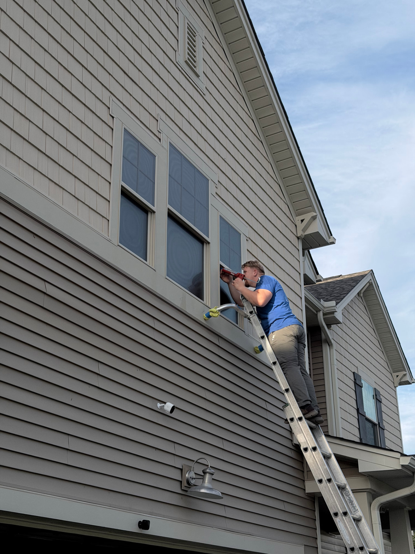 Installer on an extension ladder applying window film to a second-story residential window