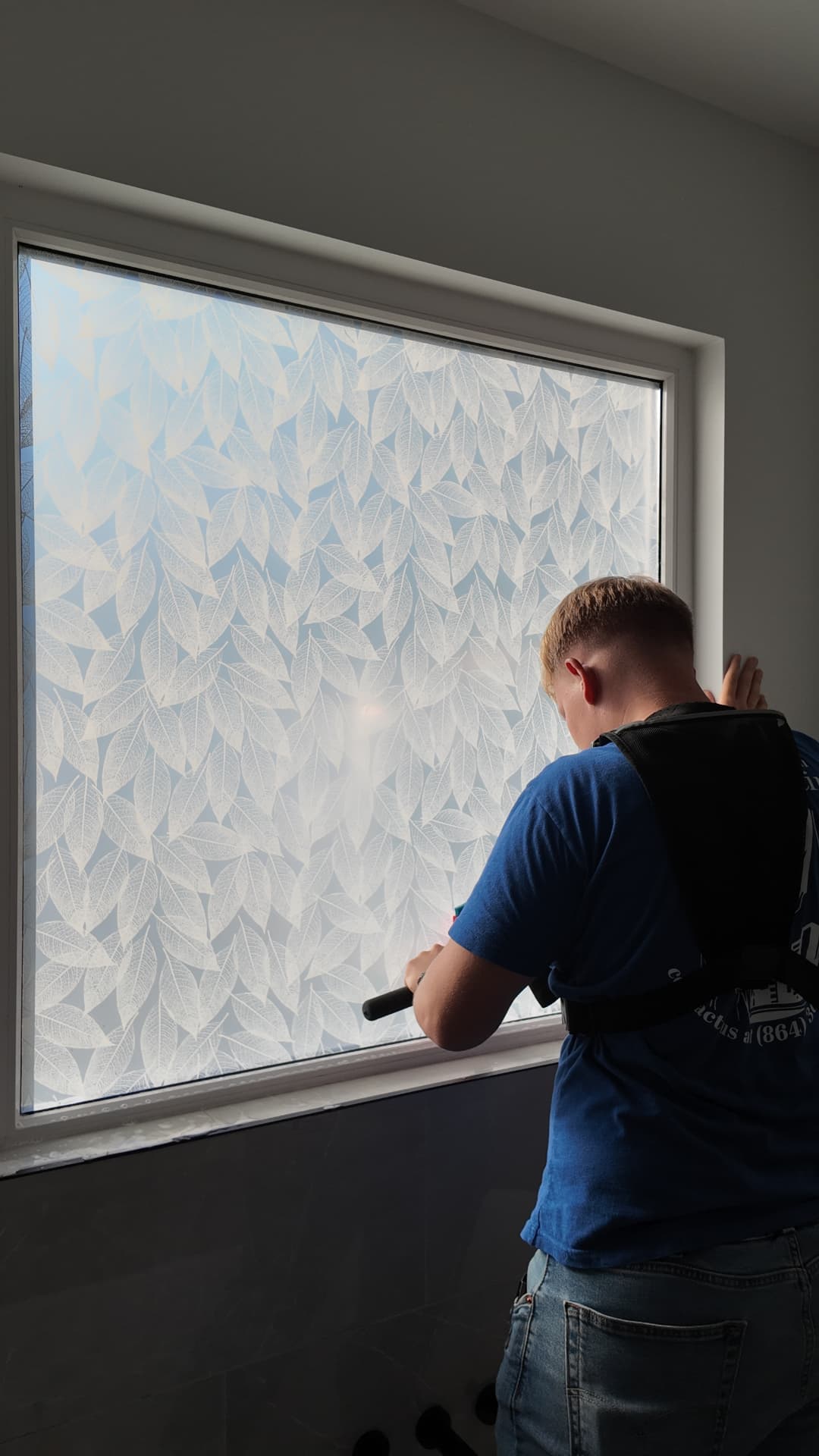 Installer applying decorative leaf-pattern privacy film to a home window